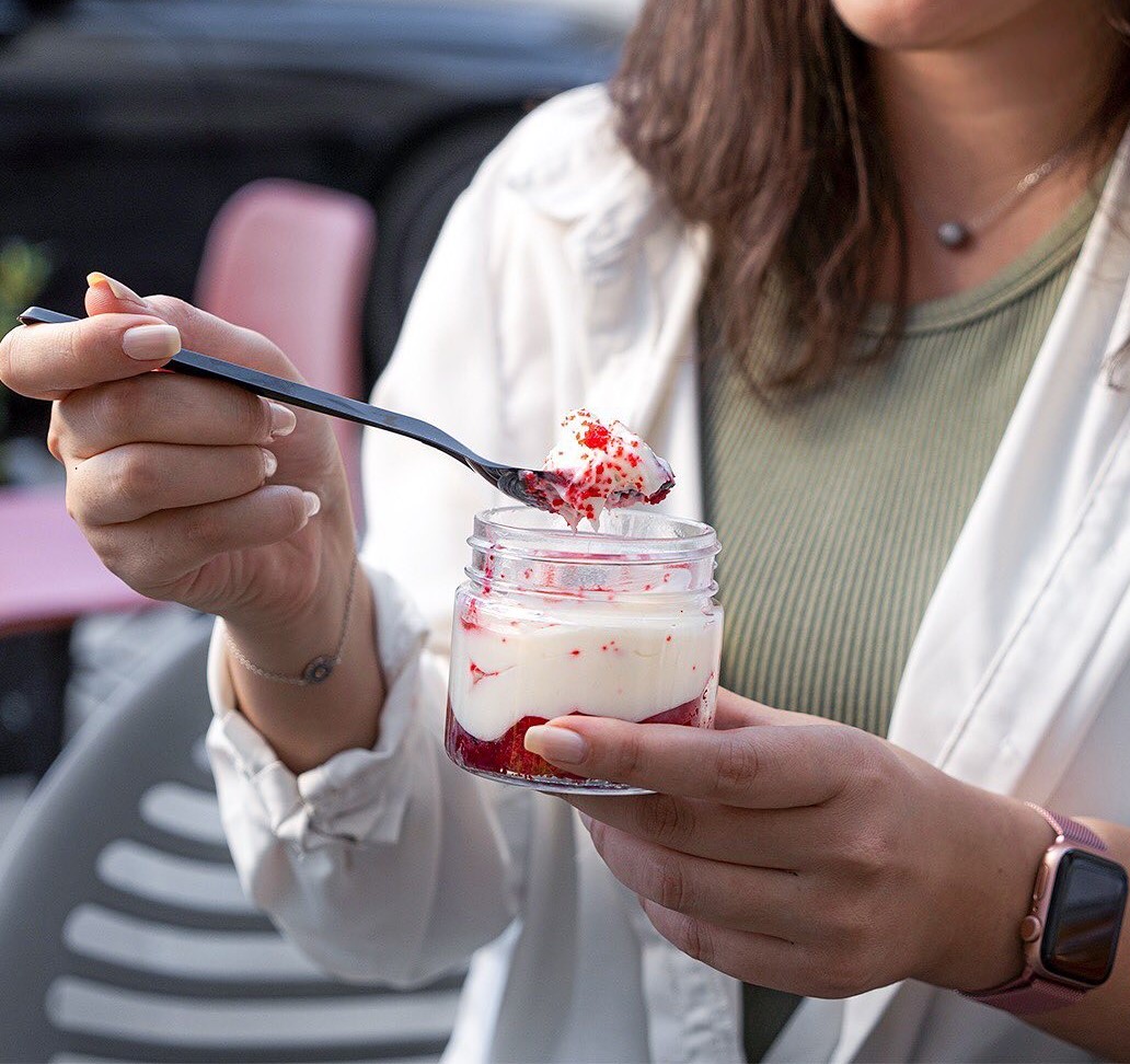 a person holding a spoon with a dessert in a jar