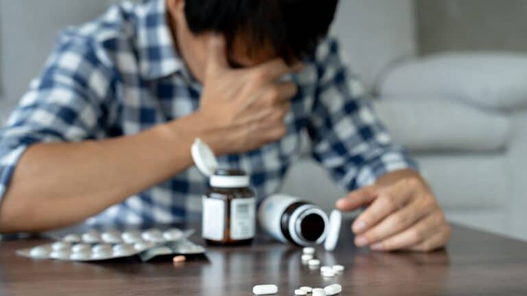 a man with his hand on his face and pills on a table