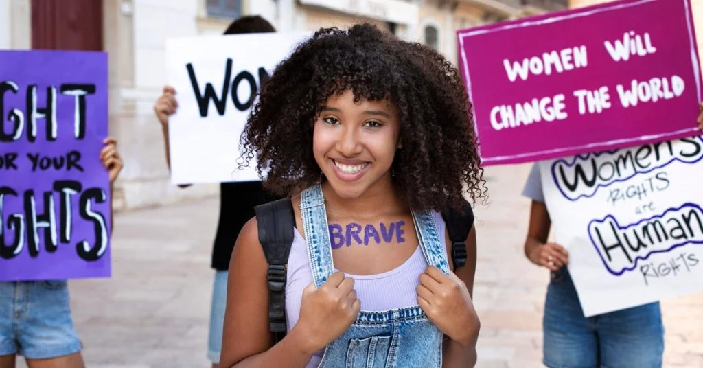 a woman with curly hair and purple backpack holding signs