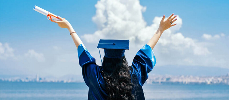 a woman in a graduation cap and gown with her hands up