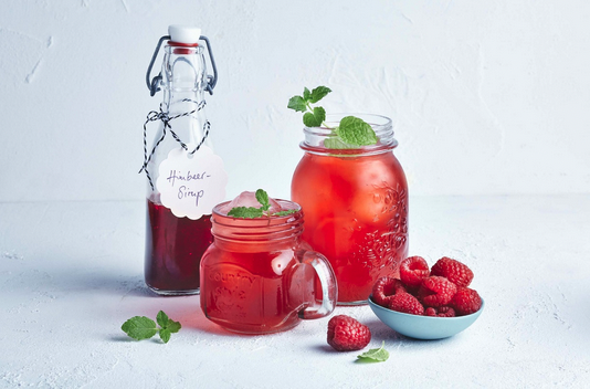 a group of jars of red liquid and a bowl of raspberries