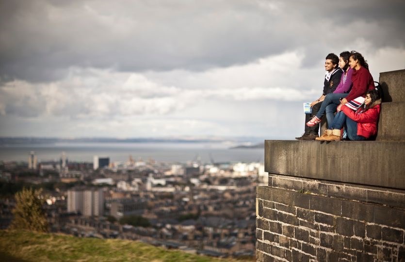 a man and woman sitting on a ledge overlooking a city