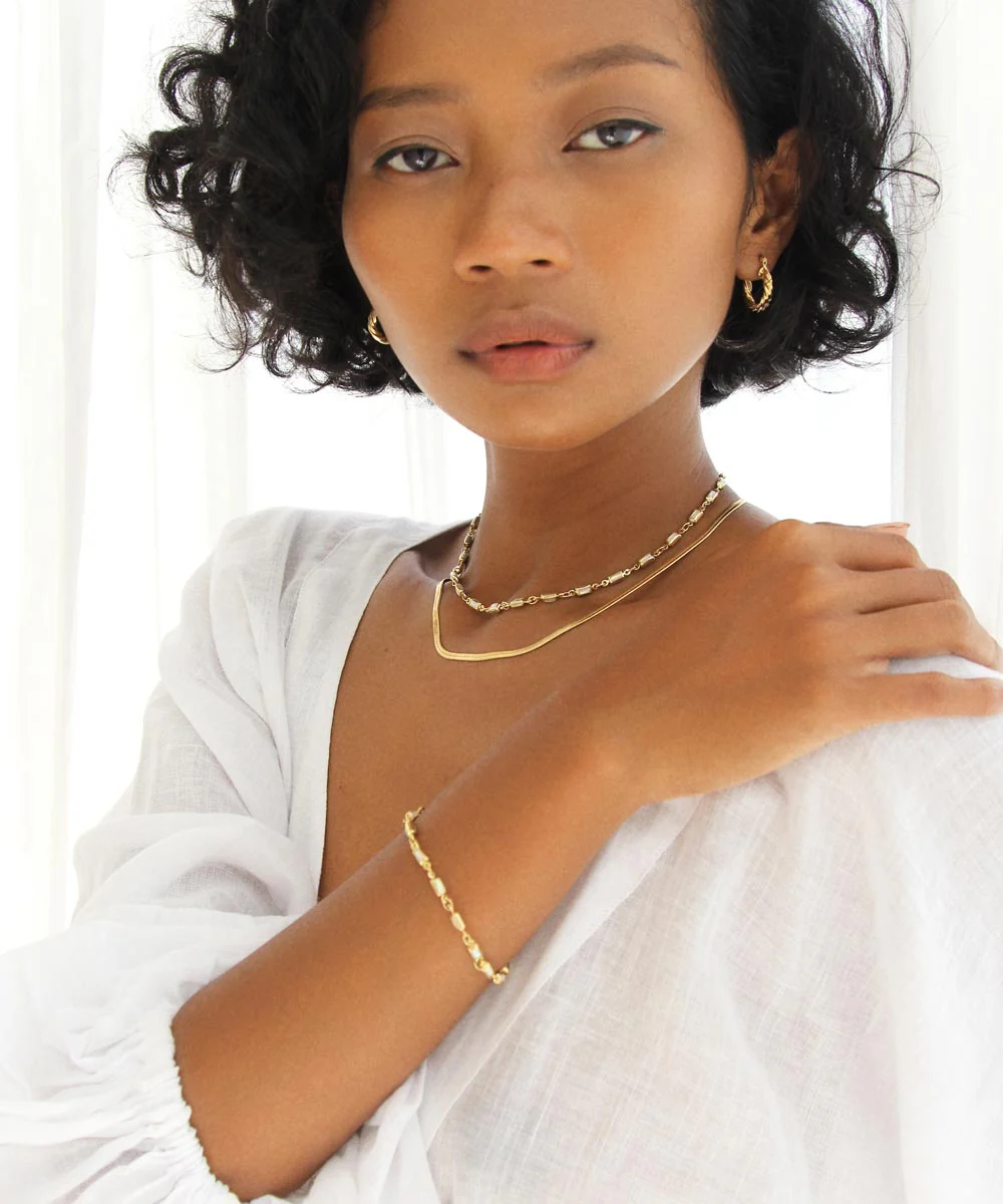 a woman with short dark hair wearing a white shirt and gold jewelry