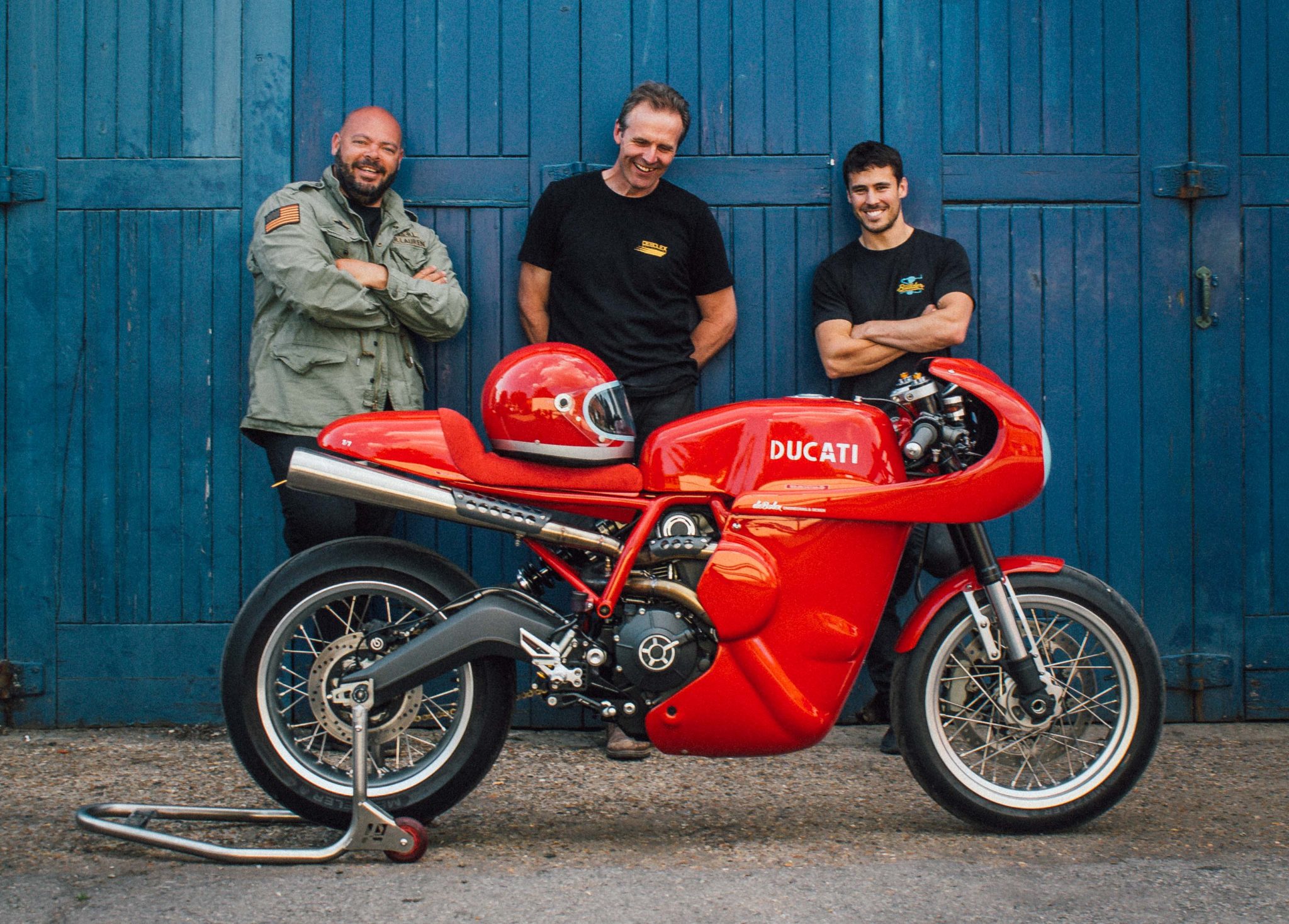 a group of men standing next to a red motorcycle