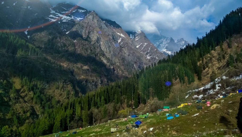 a group of tents on a hillside with trees and mountains in the background