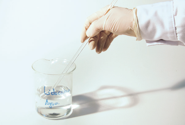 a hand holding a glass beaker with a dropper