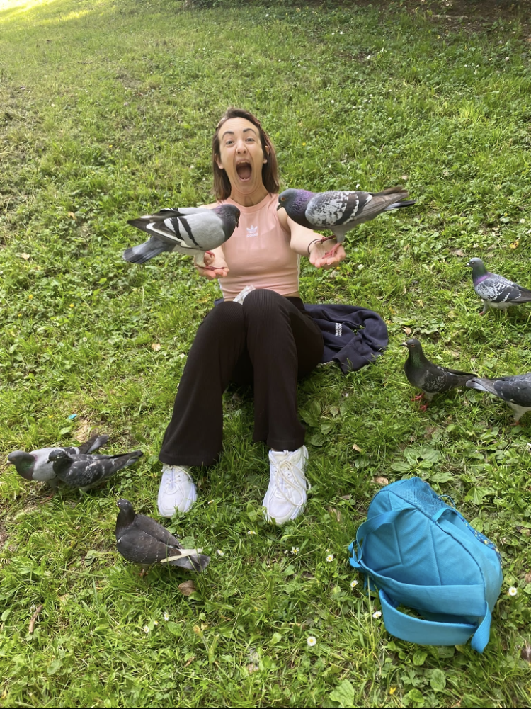 a woman sitting on grass with pigeons