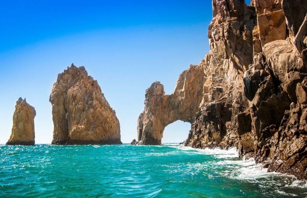a body of water with a rock arch with Arch of Cabo San Lucas in the background