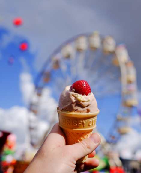 a hand holding an ice cream cone with a strawberry on top