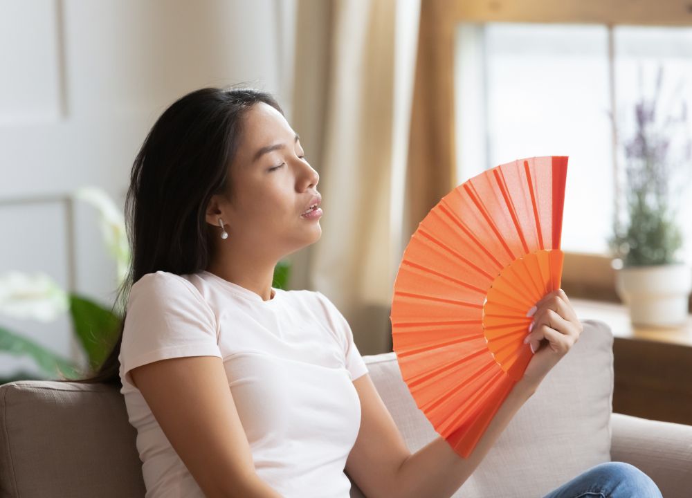 a woman sitting on a couch holding an orange fan
