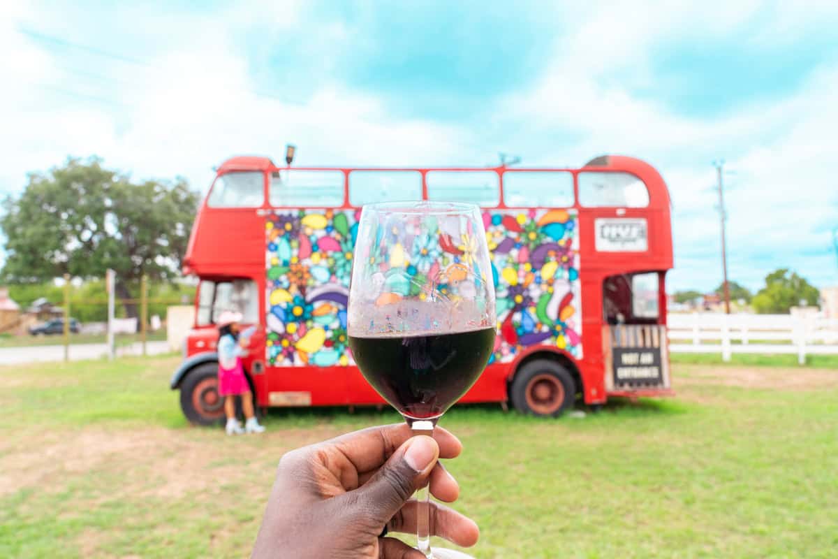 a hand holding a glass of wine in front of a bus