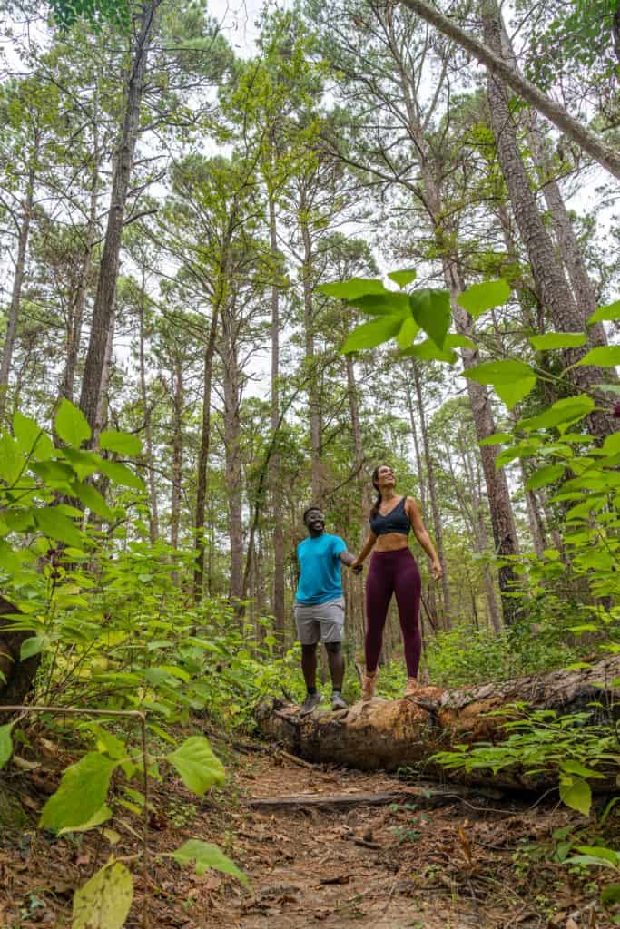 a man and woman standing on a log in the woods