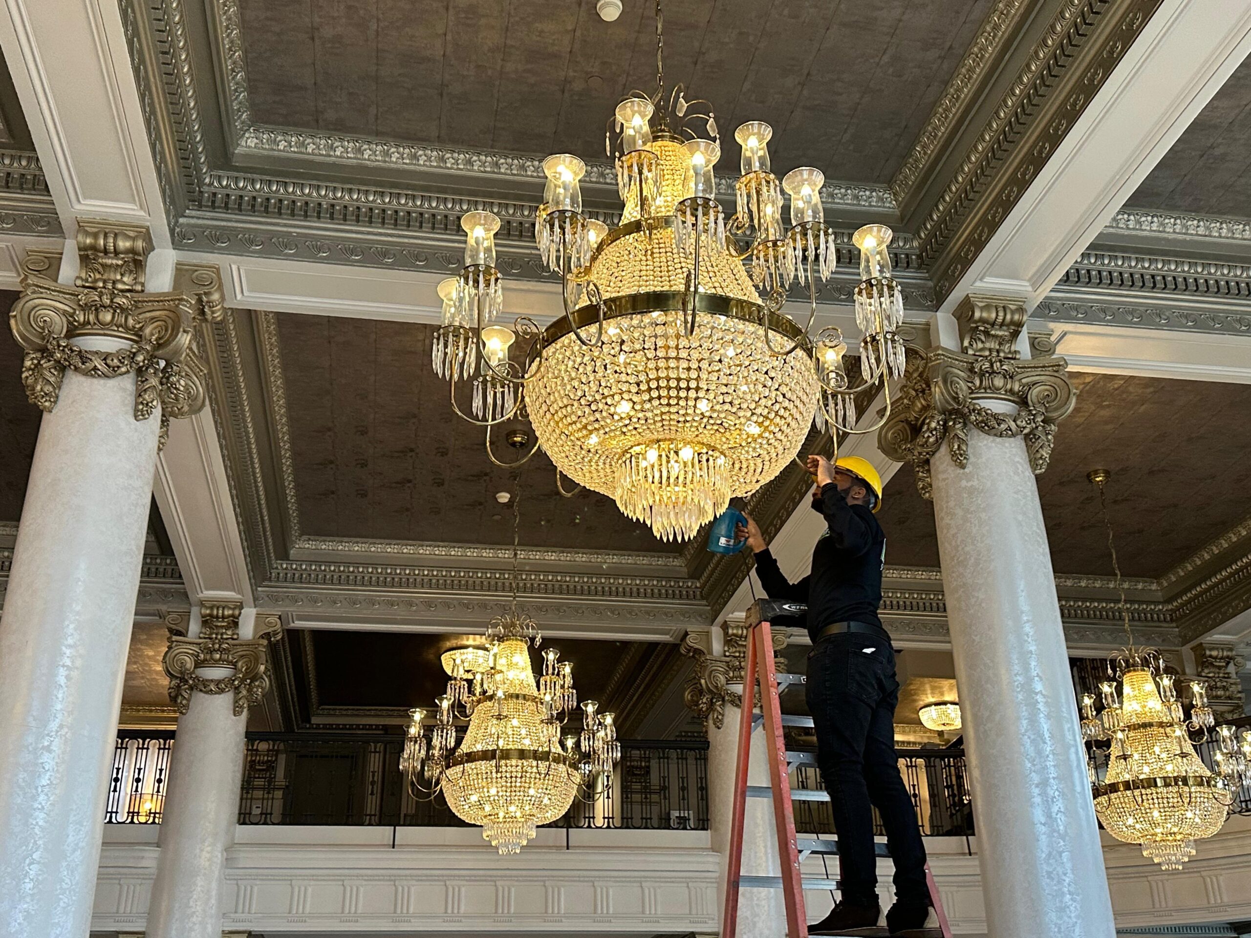 a man on a ladder in a room with a chandelier