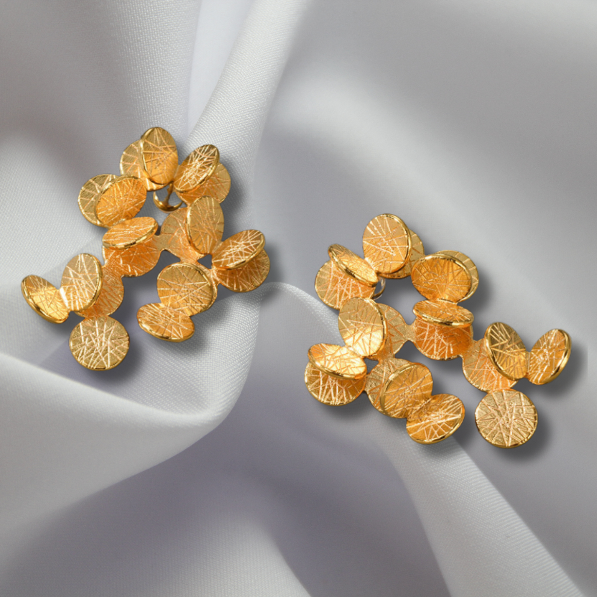 a pair of gold earrings on a white fabric
