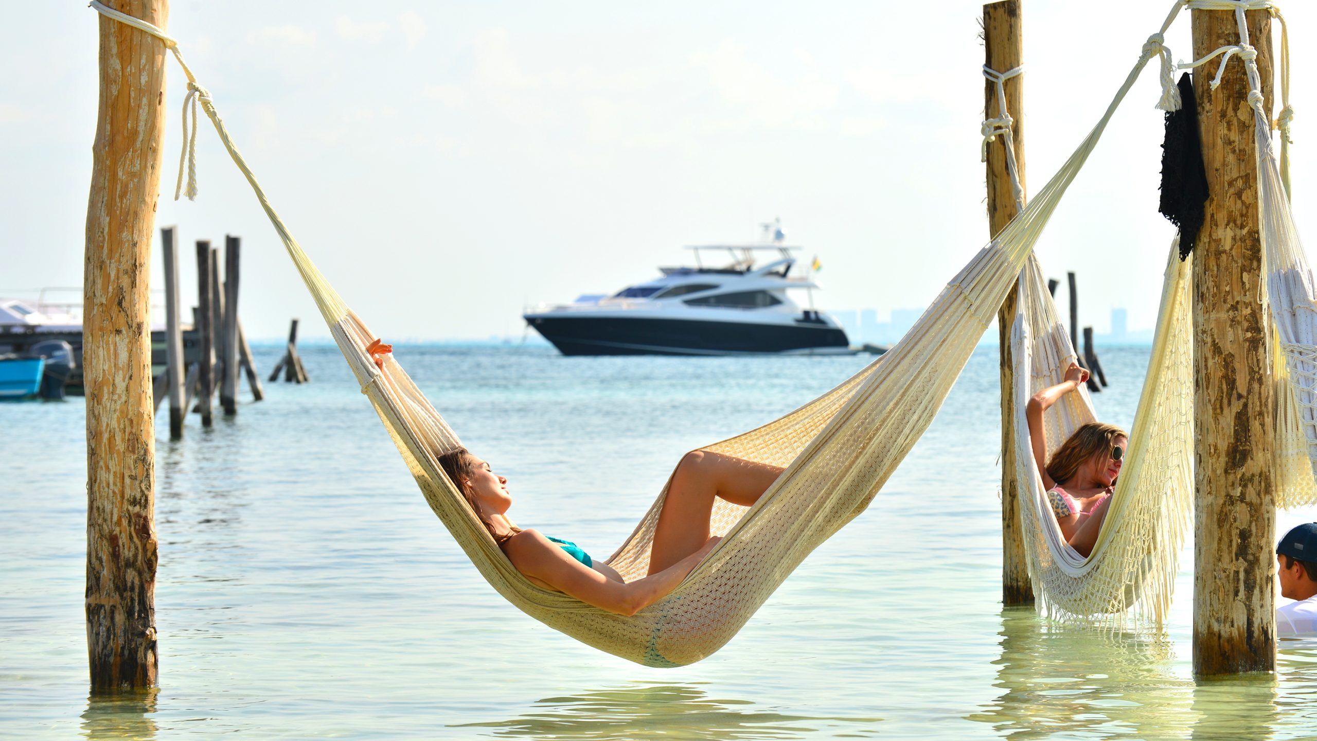 a woman in a swimsuit lying in a hammock on a beach