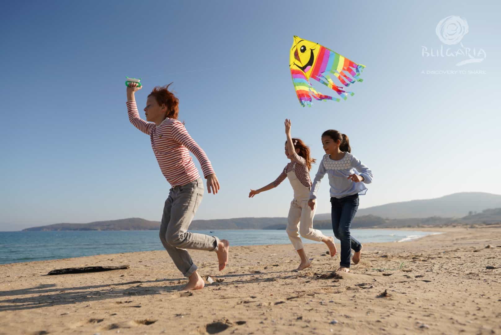 a group of kids running on a beach with a kite