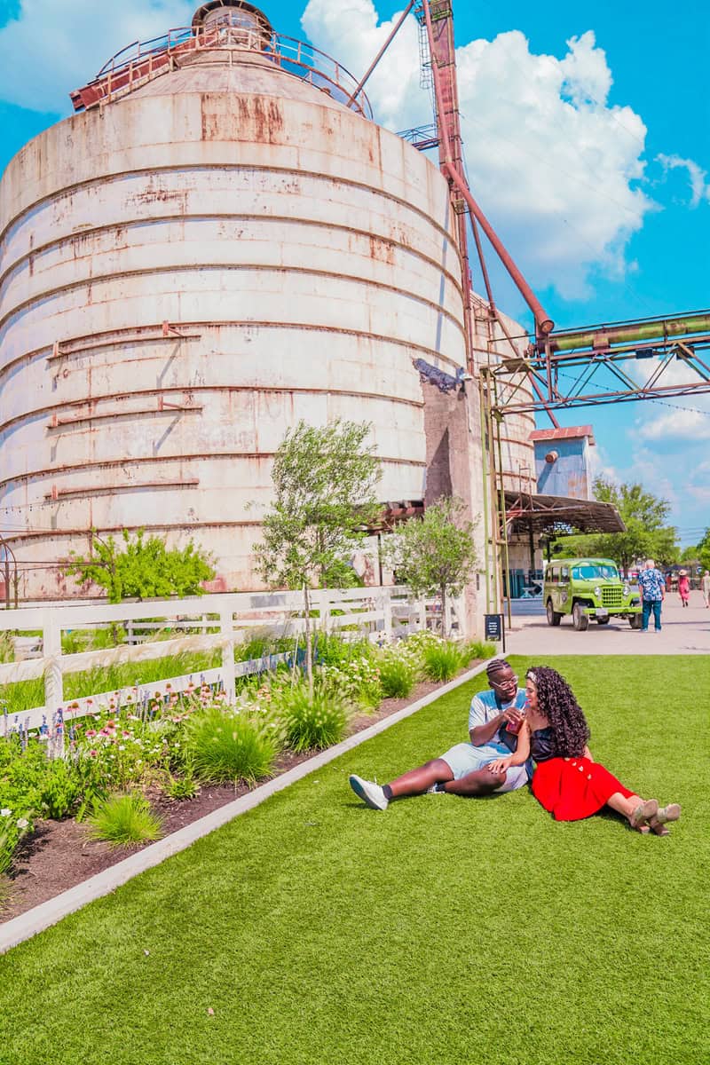 a man and woman sitting on grass next to a silo