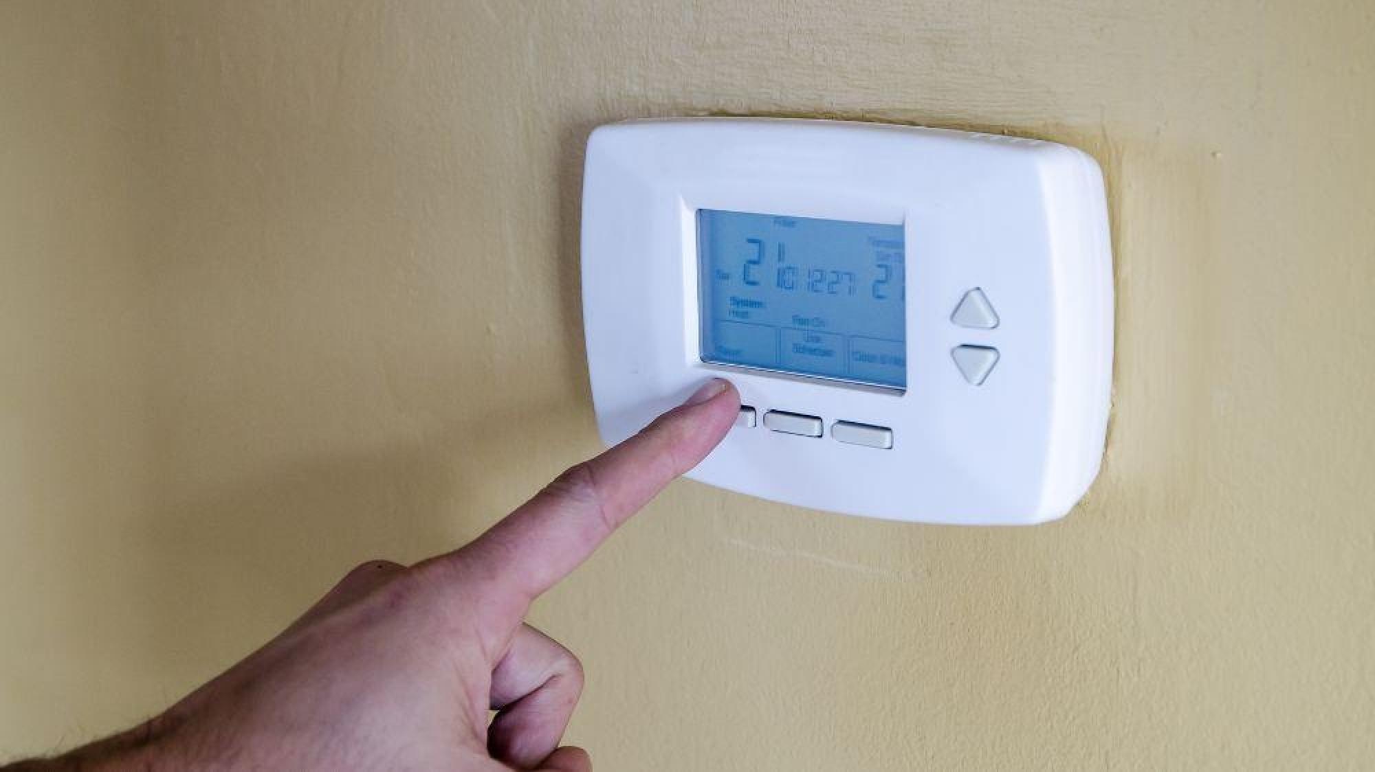 a finger pressing a screen on a thermostat