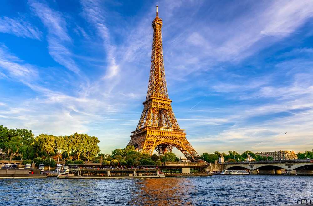 a large metal tower next to a body of water with Eiffel Tower in the background