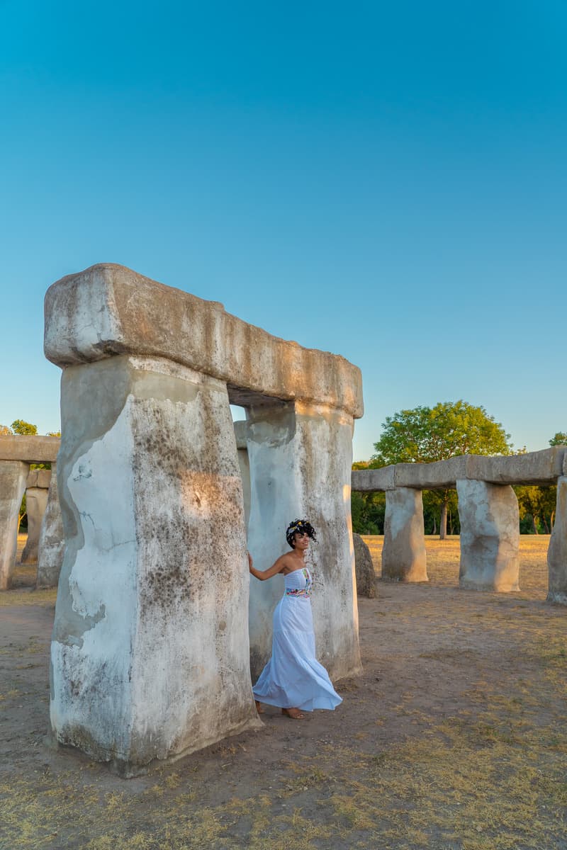 a woman in a white dress standing next to a large stone structure