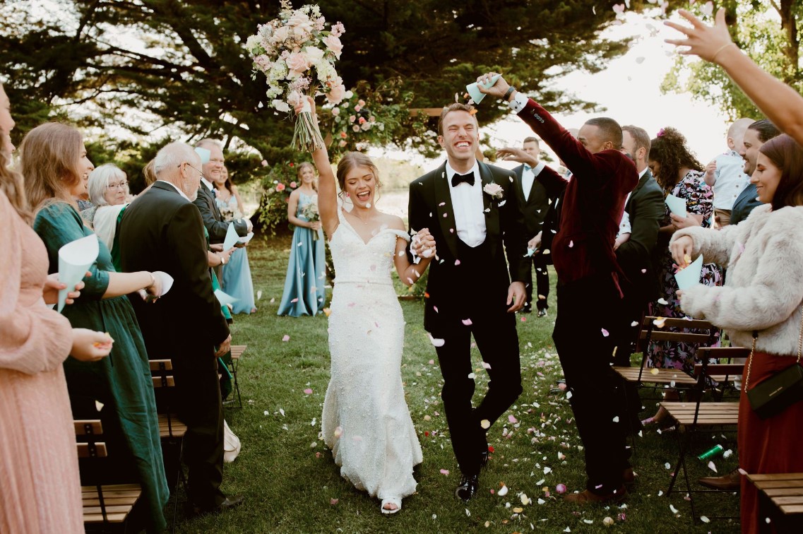 a bride and groom walking down a lawn with confetti falling down