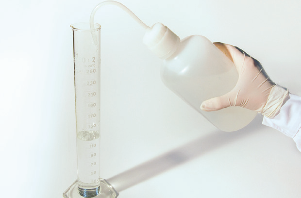 a hand holding a bottle and a measuring cylinder