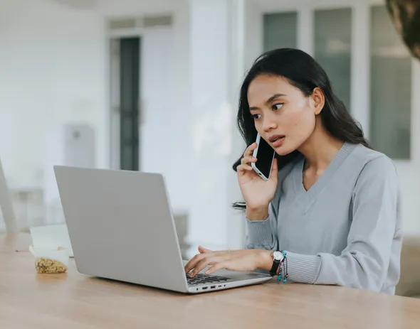 a woman talking on a cell phone while using a laptop