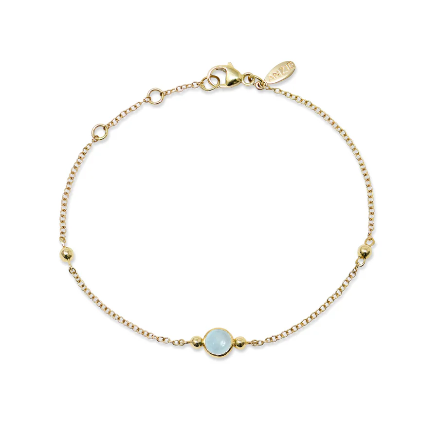 a gold chain bracelet with a blue stone and a round bead