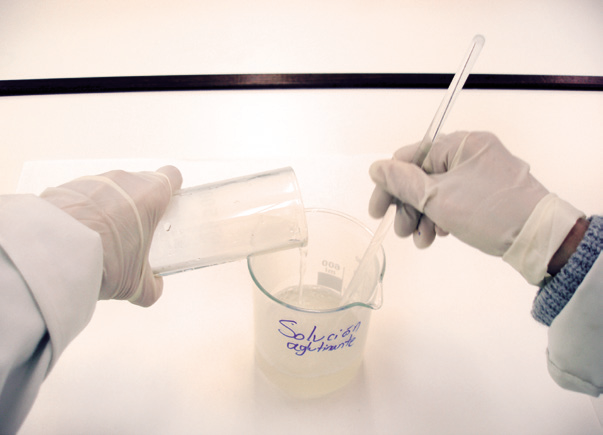 hands in gloves pouring liquid into a beaker