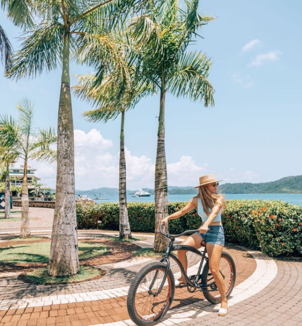 a woman riding a bicycle on a path with palm trees and water