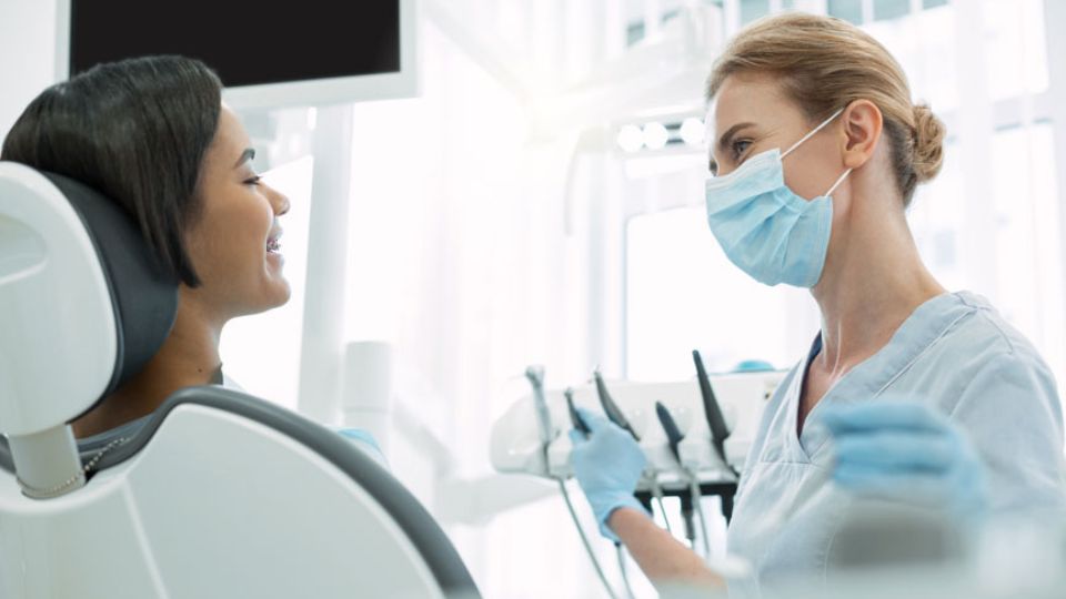 a woman wearing a mask and gloves talking to a dentist