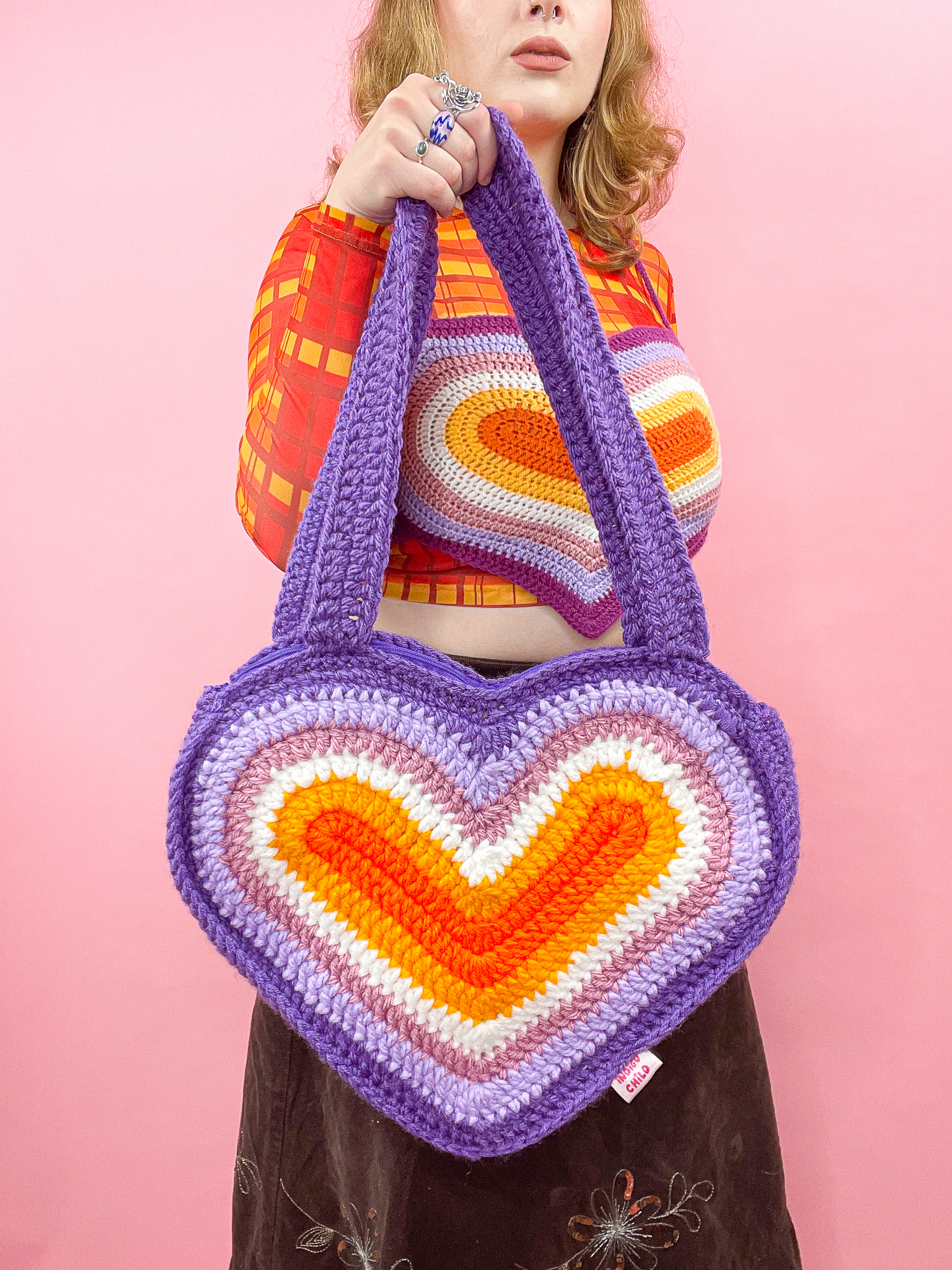 a woman holding a knitted heart shaped bag