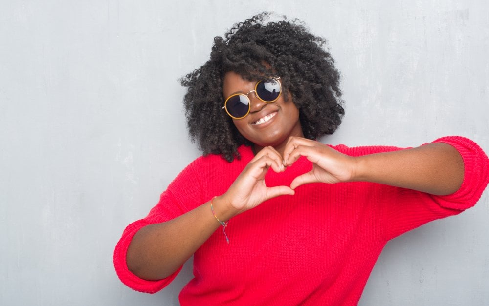 a woman wearing sunglasses and a red sweater making a heart with her hands