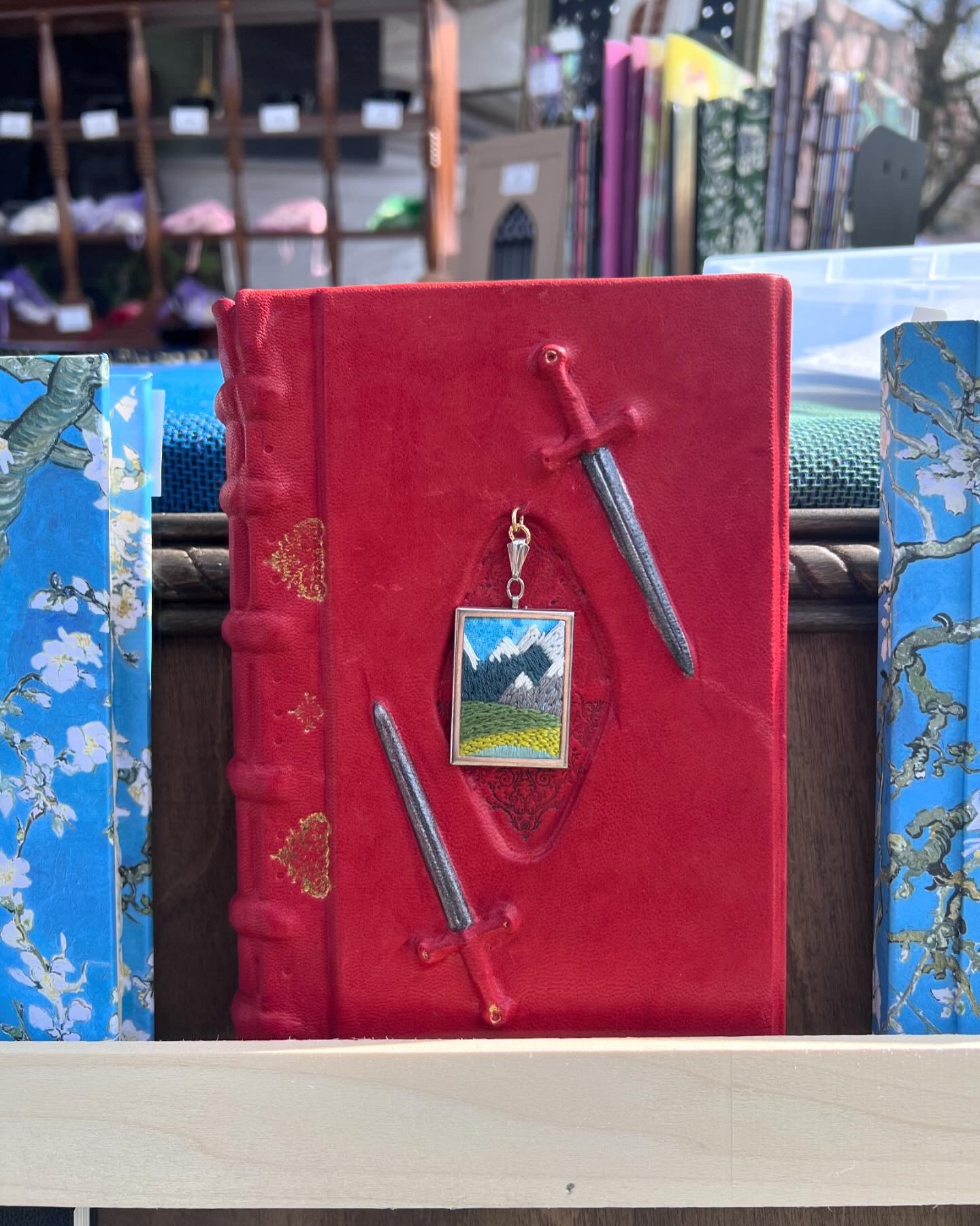 a red book with a picture of a landscape and two swords