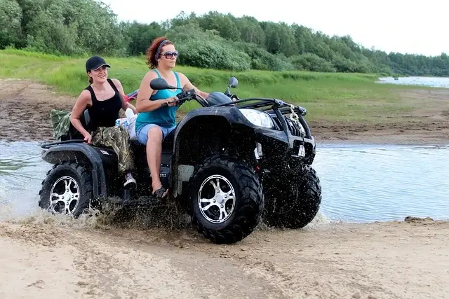 two women riding a four wheeler on a muddy beach