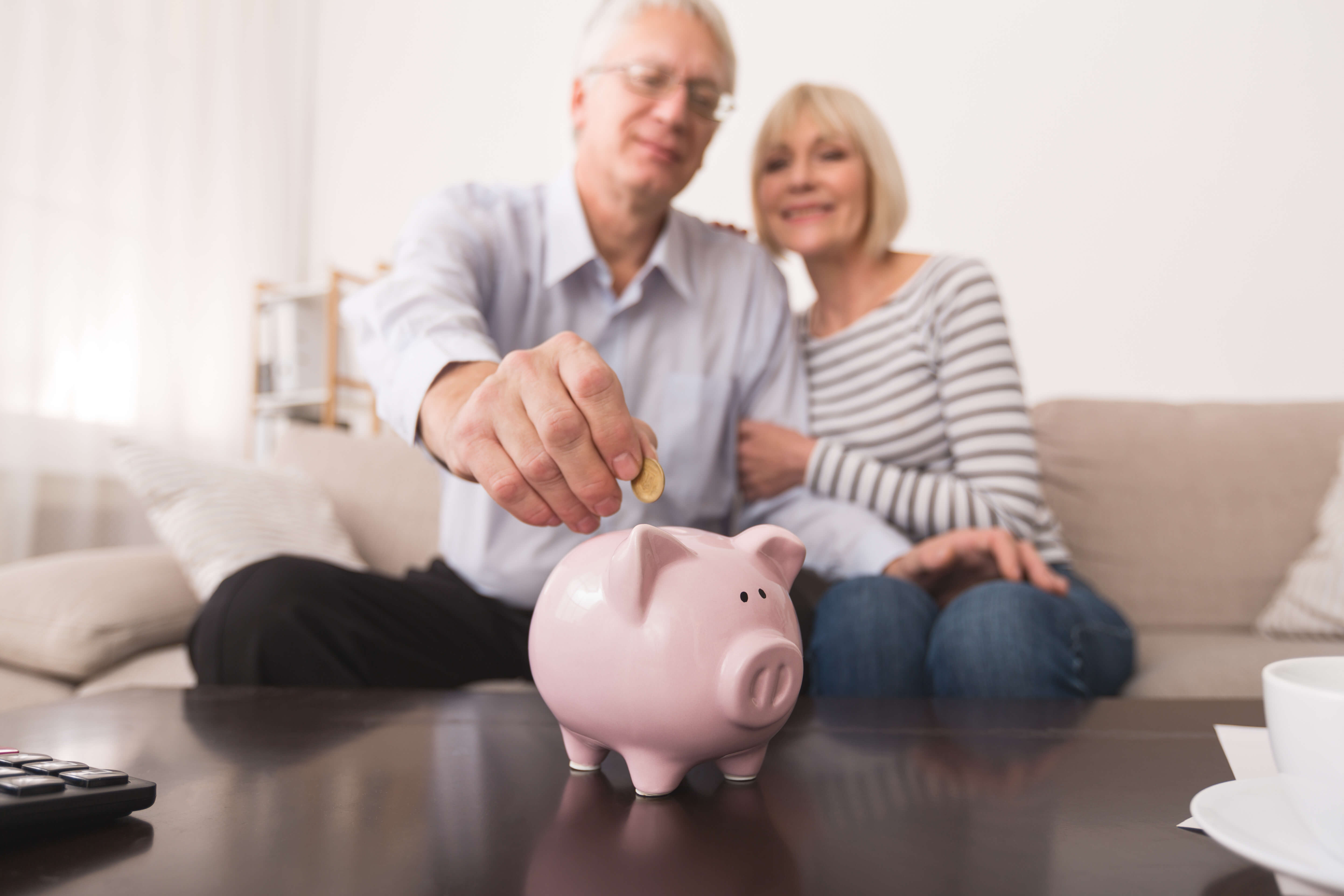 a man and woman sitting on a couch putting a coin into a piggy bank
