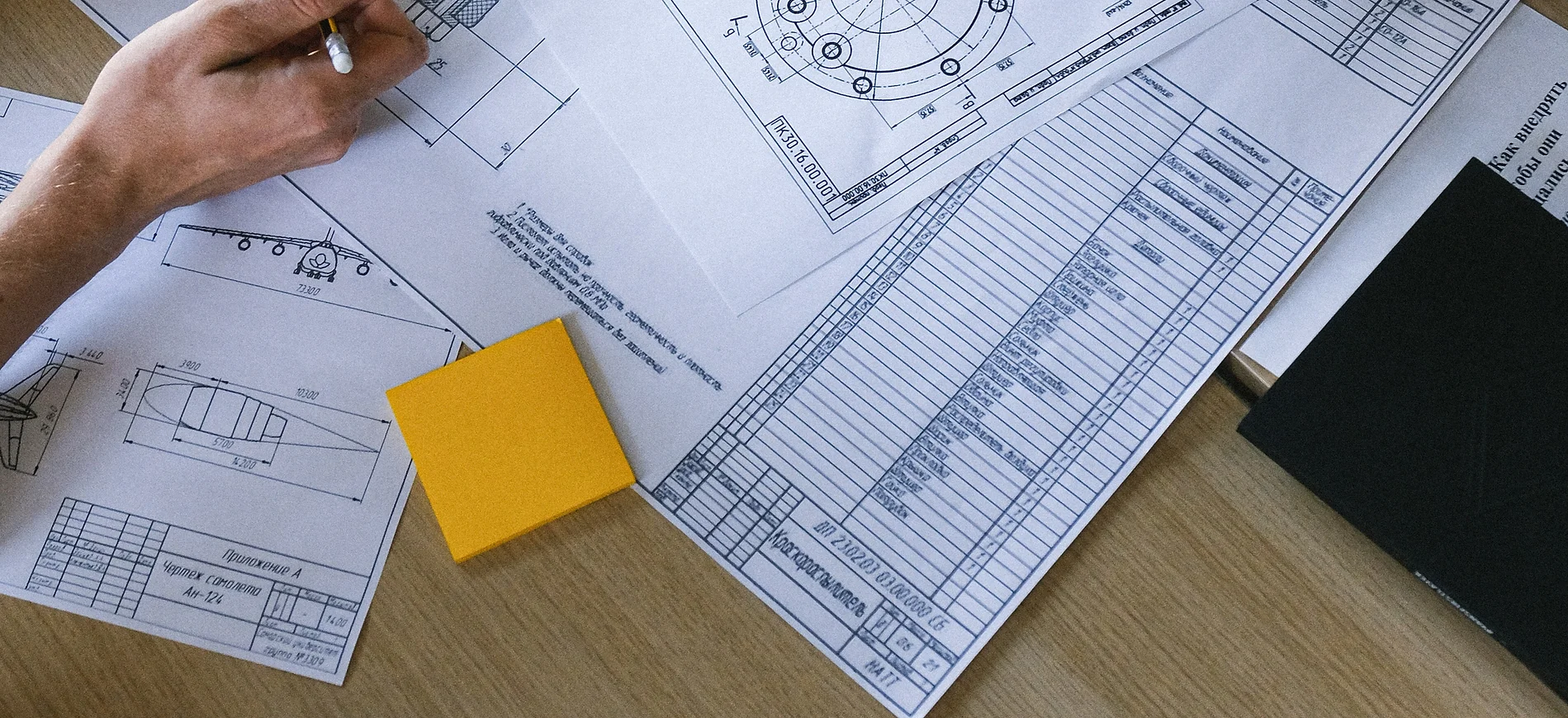 a hand holding a yellow post-it note next to a blueprint