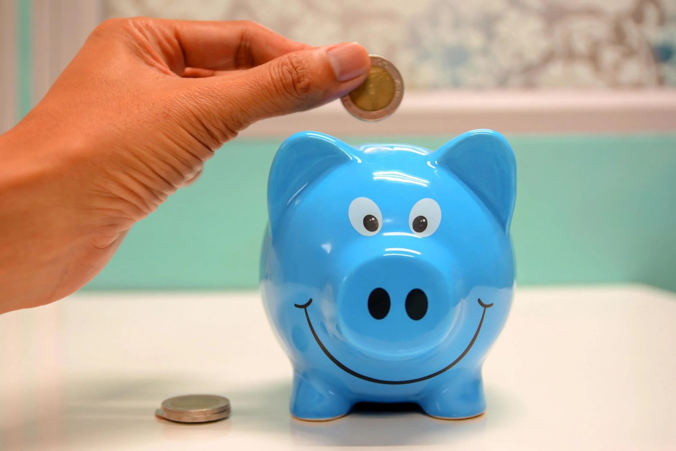 a hand putting a coin into a blue piggy bank