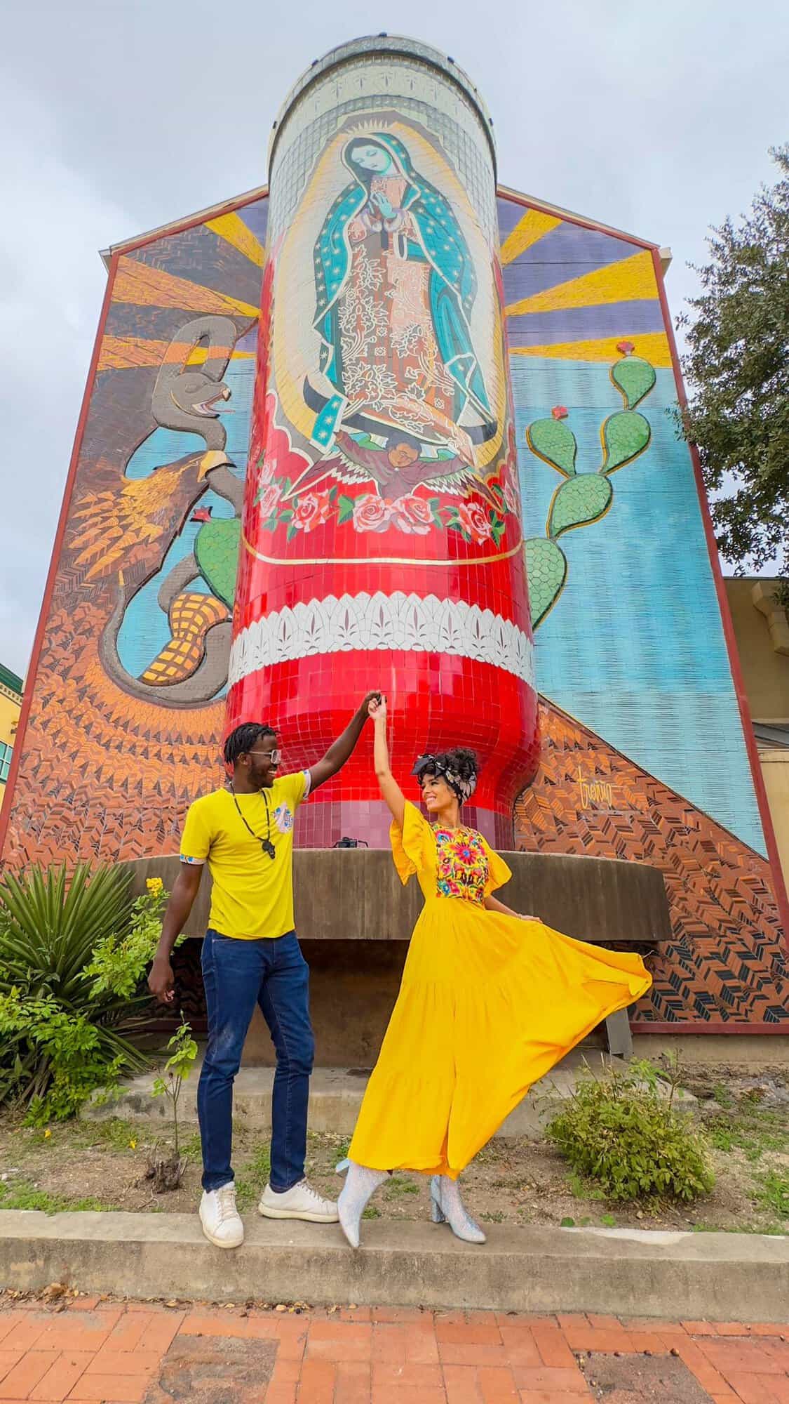 a man and woman posing for a picture in front of a mural