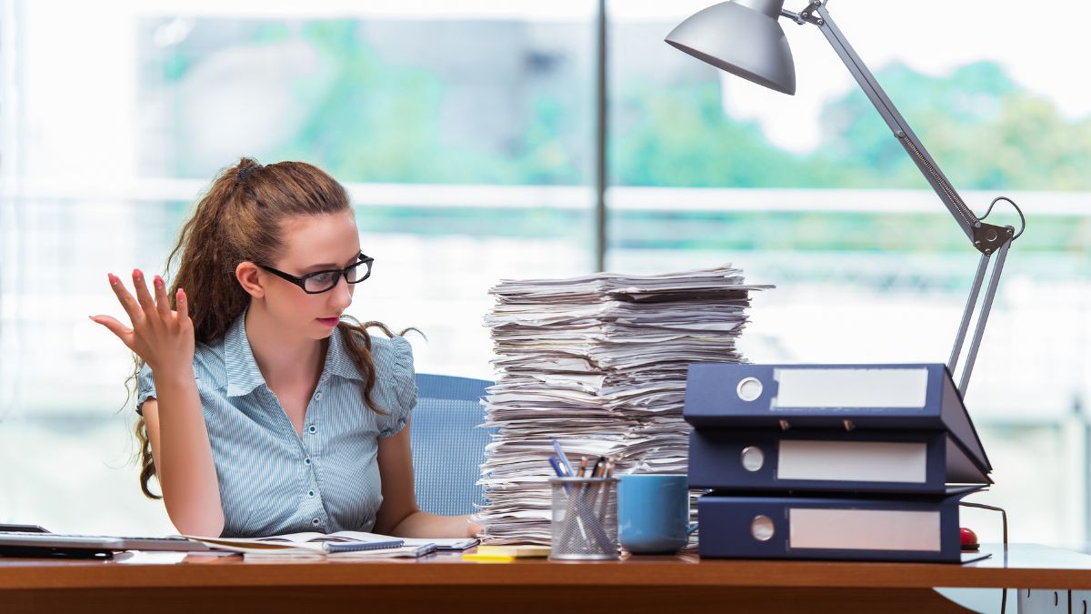 a woman sitting at a desk with a stack of papers