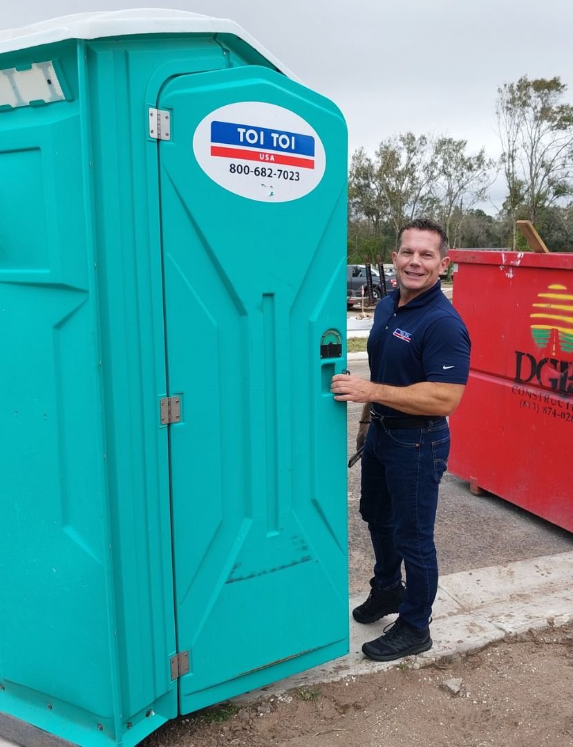 a man standing next to a blue portable toilet