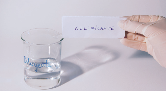 a hand holding a piece of paper next to a glass of water