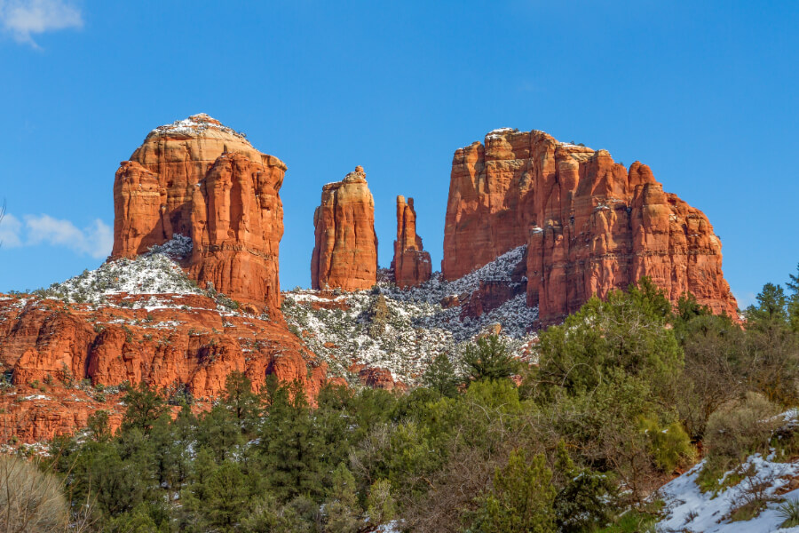 a red rock formation with snow on the top with Cathedral Rock in the background