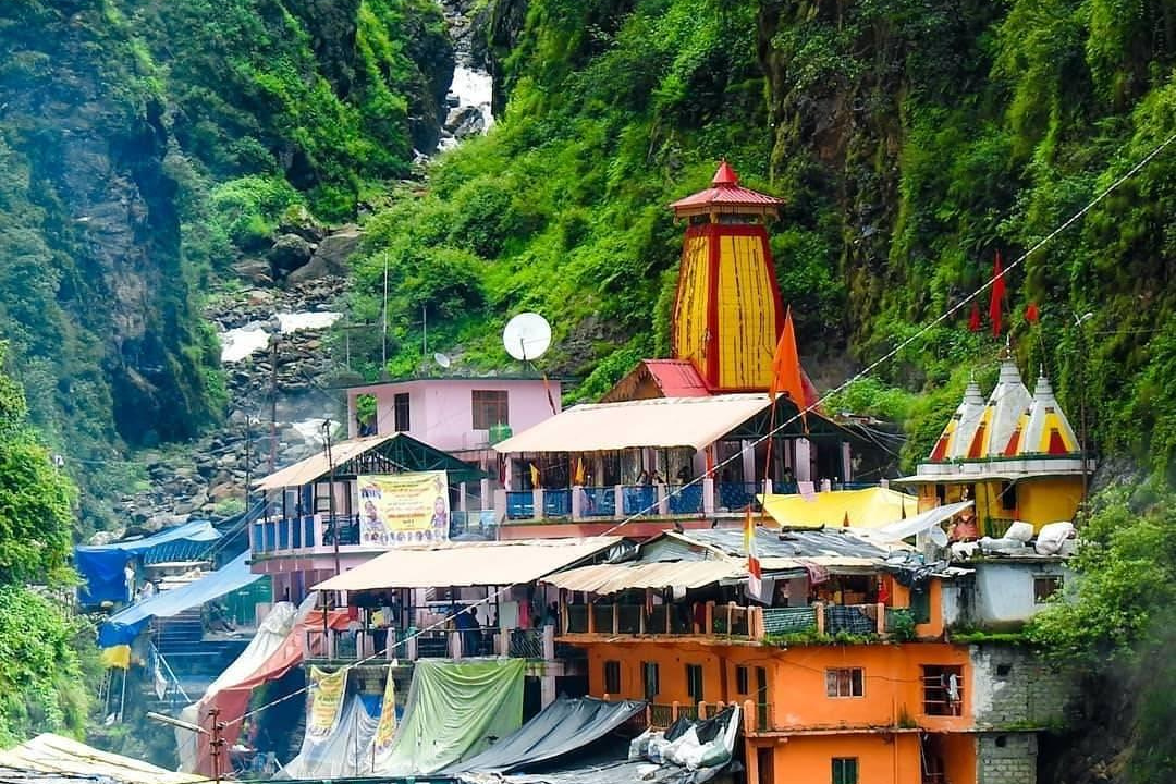 a group of buildings with a steep hillside with Yamunotri Temple in the background