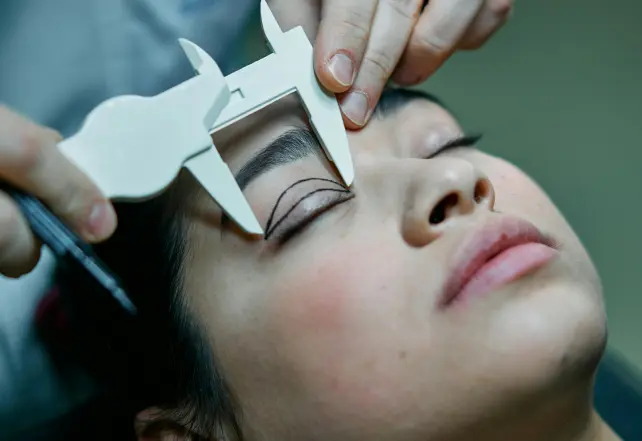 a person measuring a woman's eyebrows