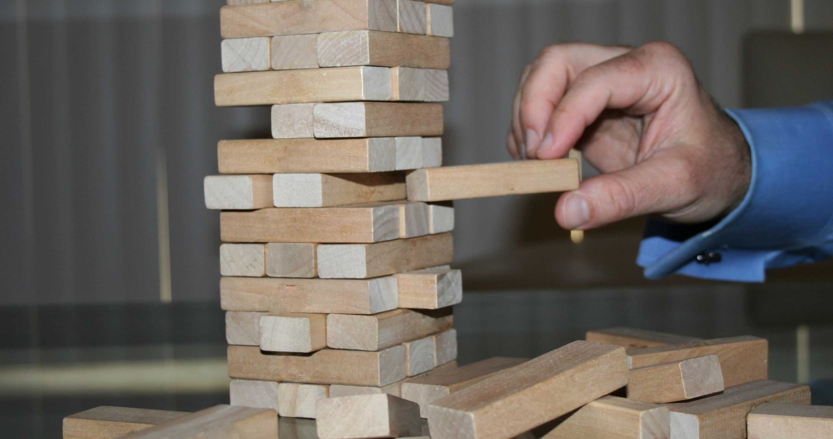 a hand placing a block on a tower of wooden blocks