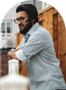 a man with a beard and glasses leaning on a white fence