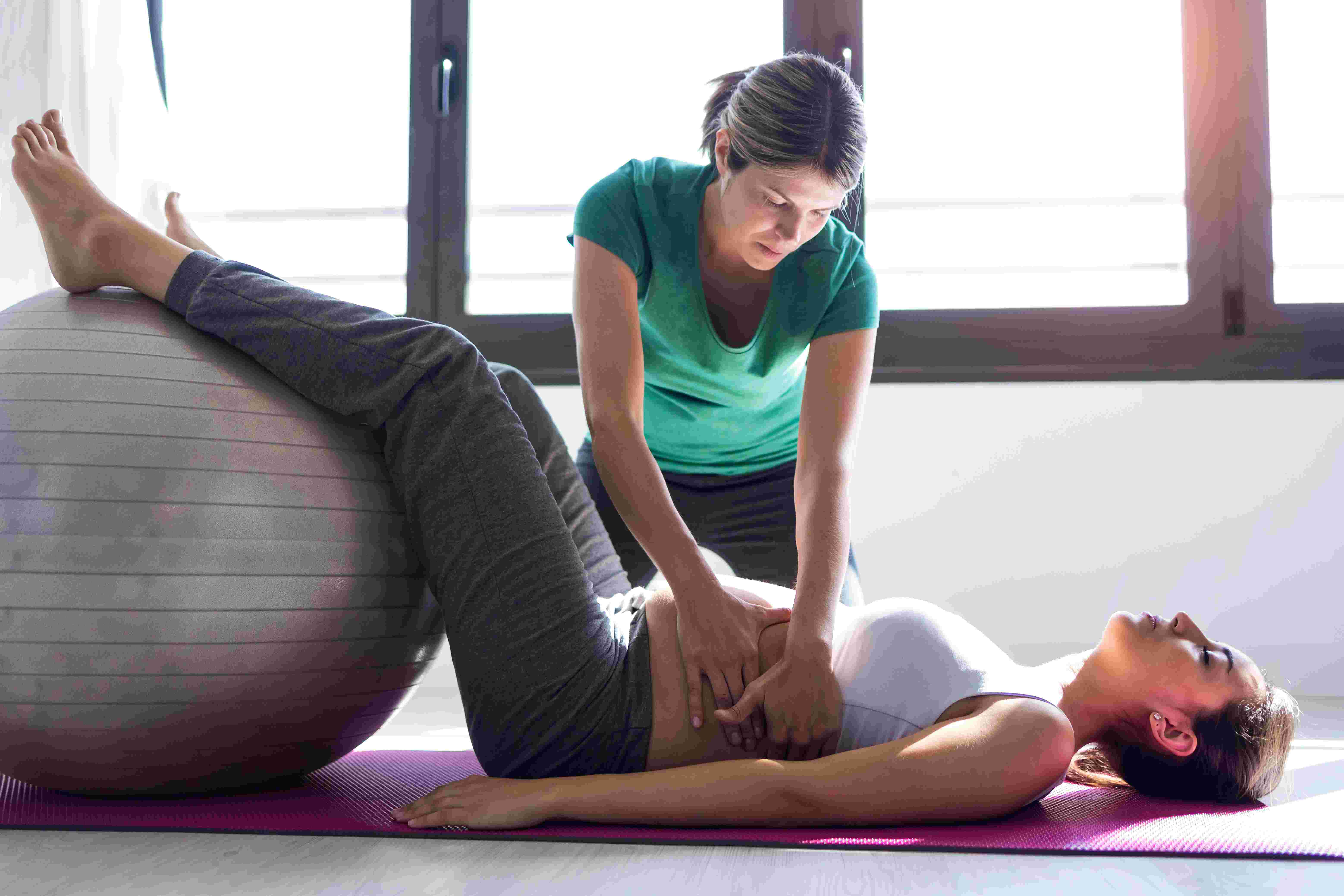 a woman lying on a mat with a ball and a woman holding her stomach