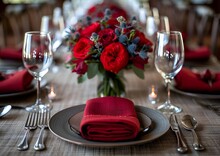 a table set with red flowers and glasses