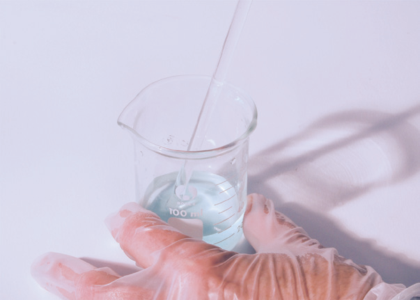 a hand in a plastic glove holding a beaker with a pipette